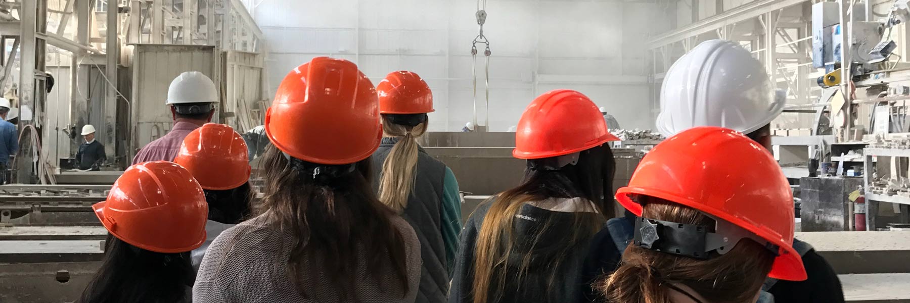 People in hard hats look at something in a factory.