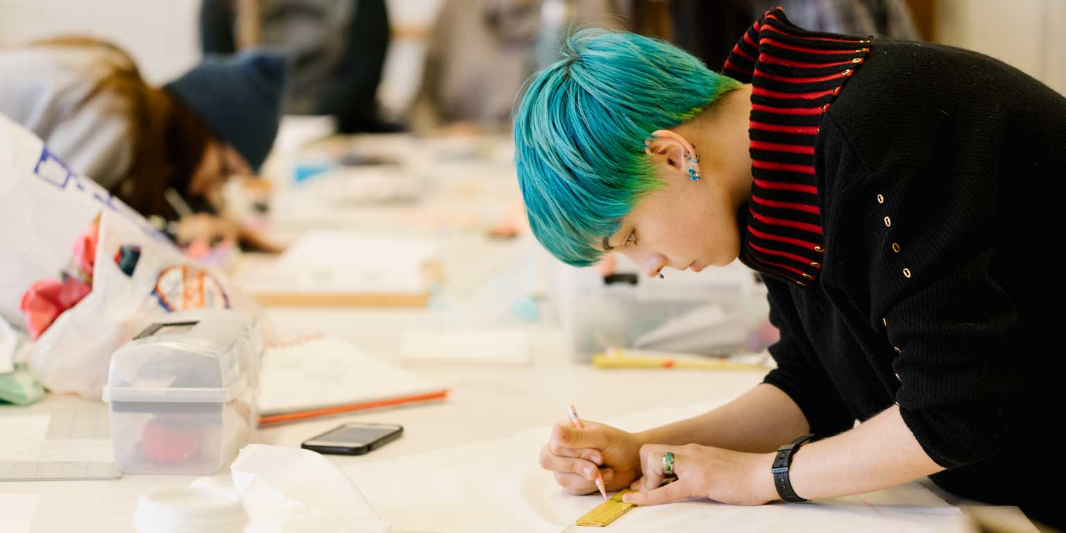 A student with blue hair works on a long table.