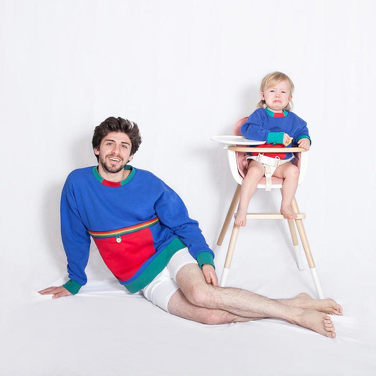 An adult and a child in a high chair look at the camera wearing matching sweaters.