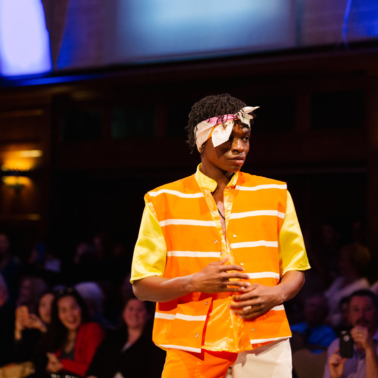 A person in an orange outfit on the runway.