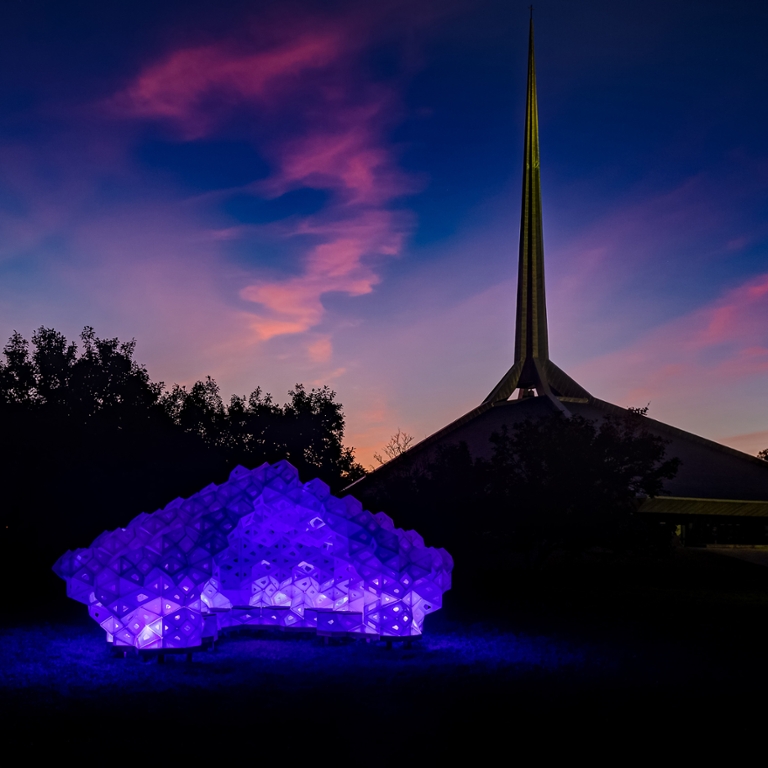 A purple sculpture lit up at dusk.