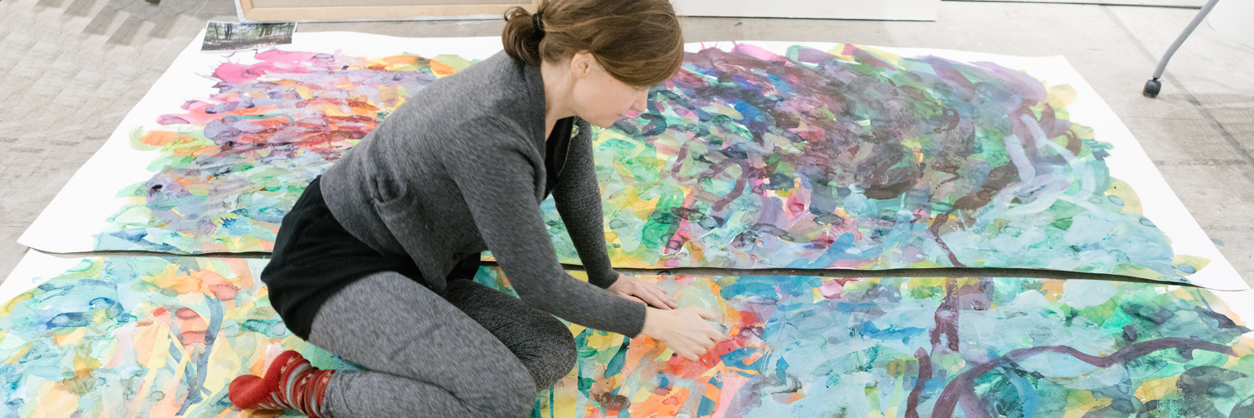 A person works on a large painting on the floor.