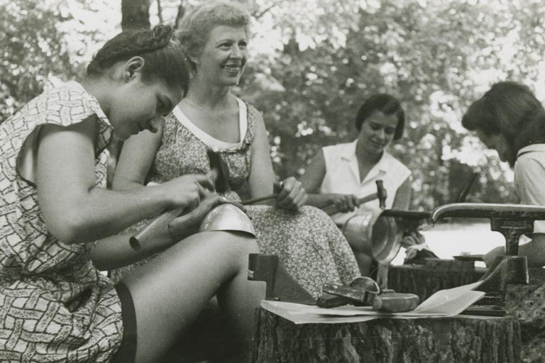 A professor teaches a group of students metalsmithing techniques outdoors. 