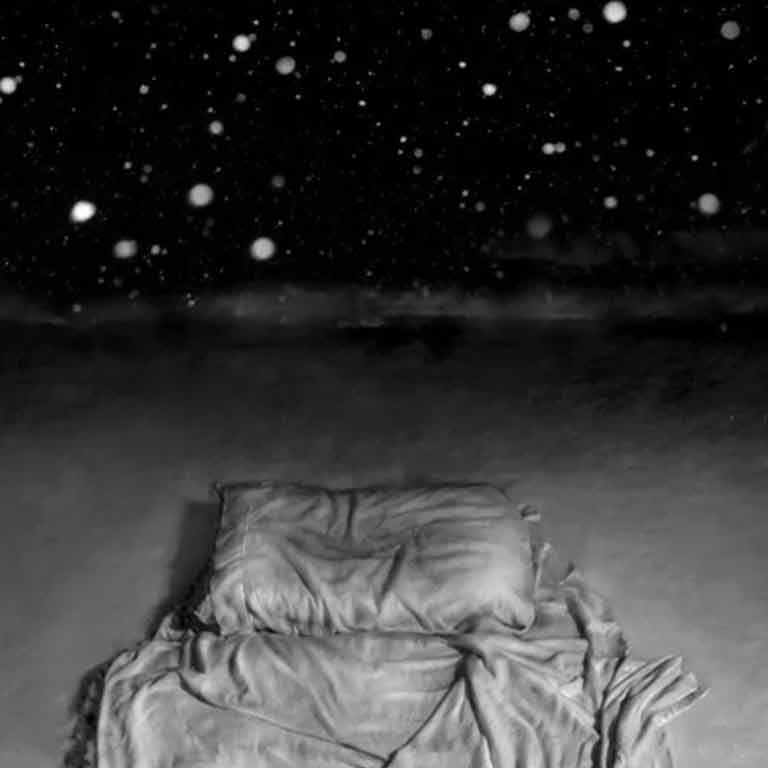 Snowy dark sky above a pillow and blanket. 