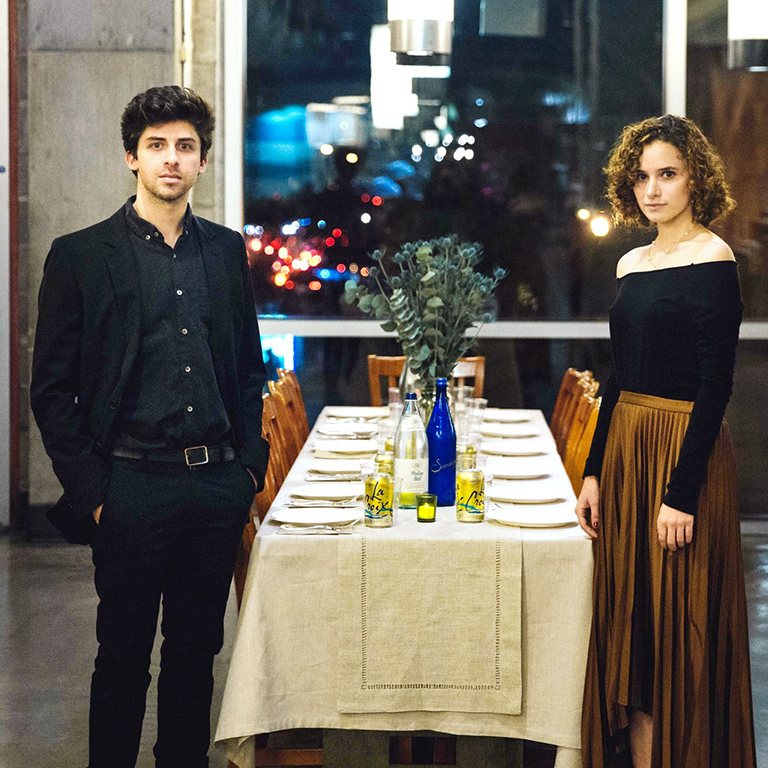 Two people stand next to a dining table set for 10.