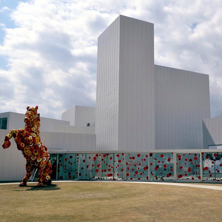 A white building with a sculpture of a horse covered in flowers in front of it.