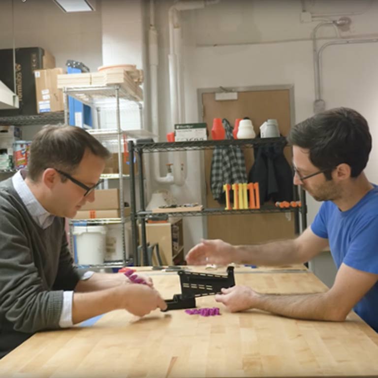 Two people sit at a table working on a prosthetic arm.