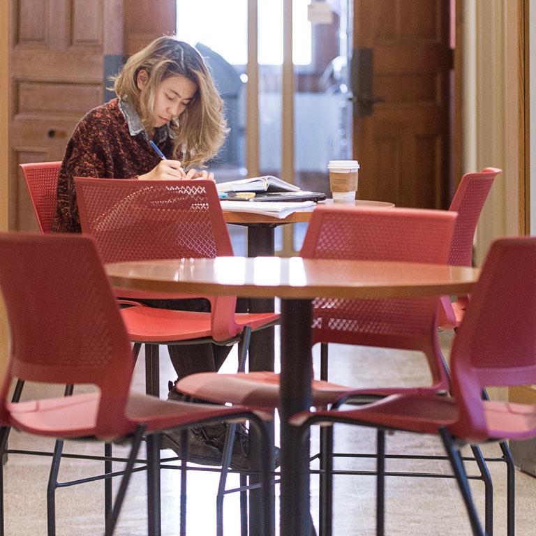 A person studies at a table with red chairs.