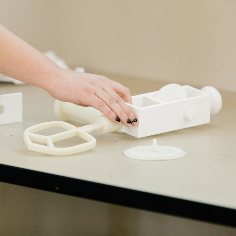 A person reaches for a white 3D printed object.